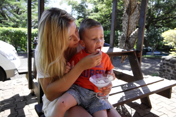 A young woman feeding a toddler boy at a picnic table