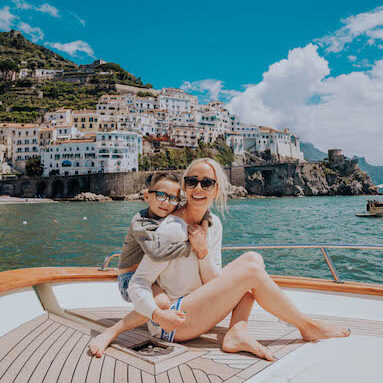 Kam and son on boat deck with Positano hillside village on Amalfi Coast Italy in background