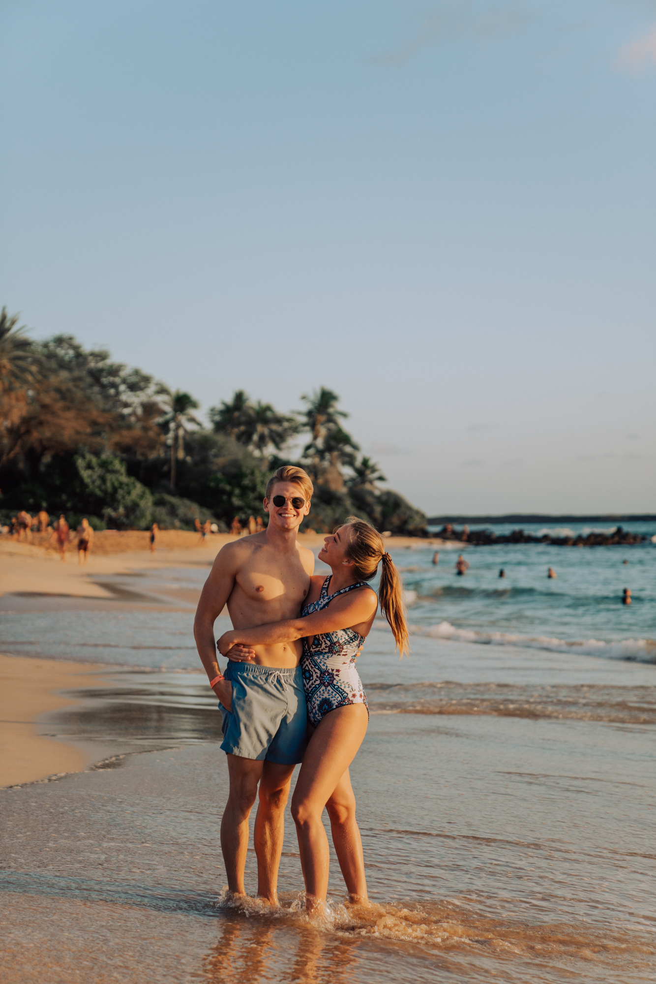 Man and woman are hugging, standing in the waves of a beach.