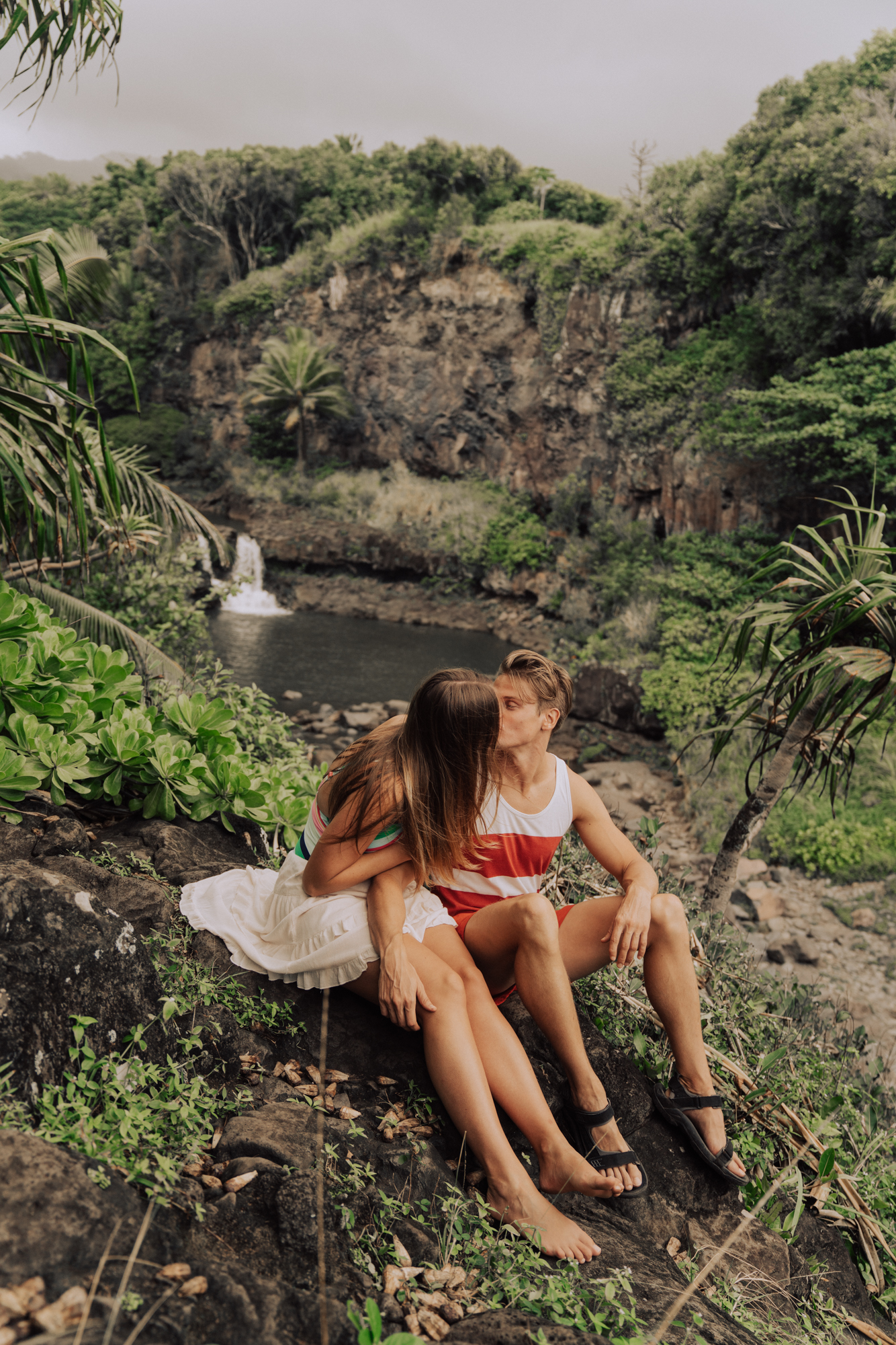 man and women kissing with a waterfall and palm trees in the background.