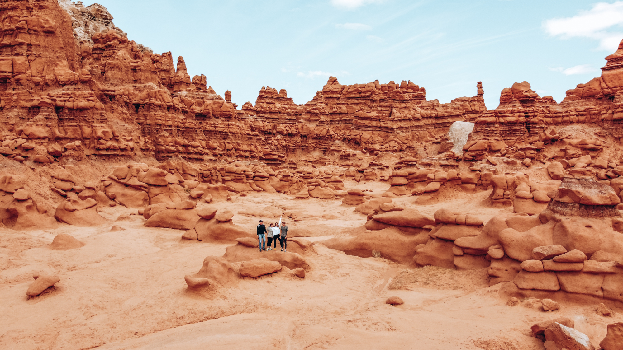 Four people can be seen in the foreground of an image with red rocks and cliffs!