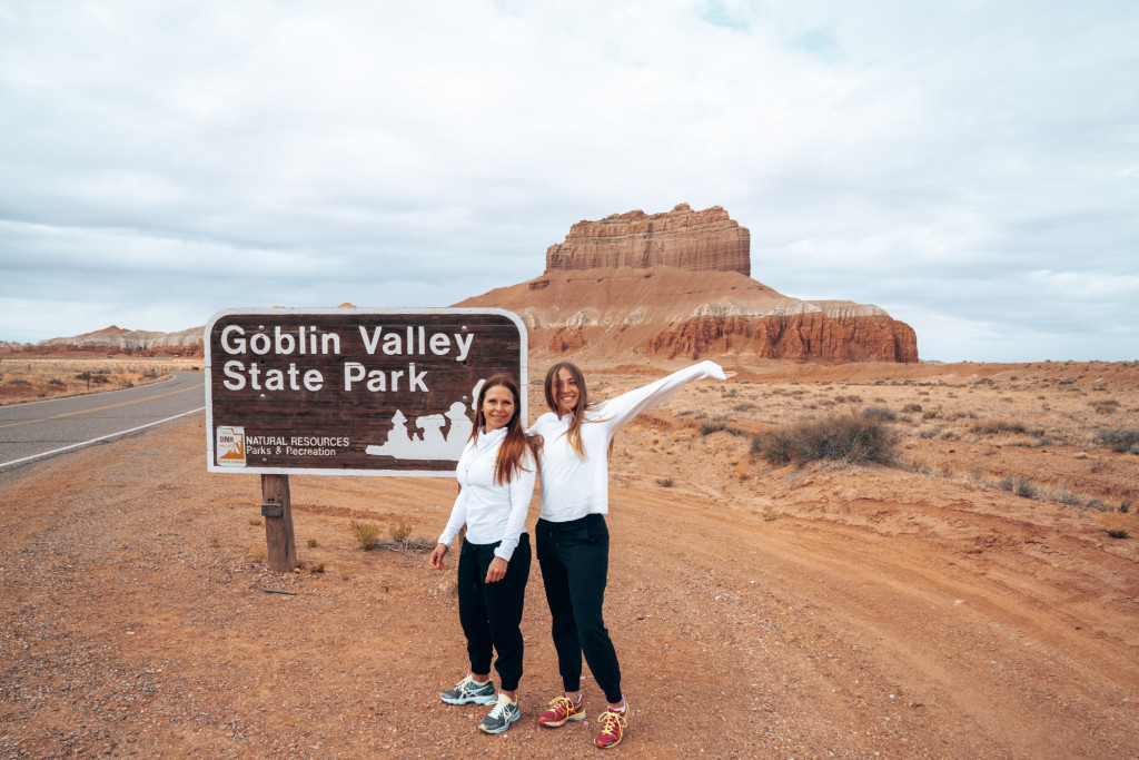 Two women standing in front of the Goblin Valley State Park with arms up.