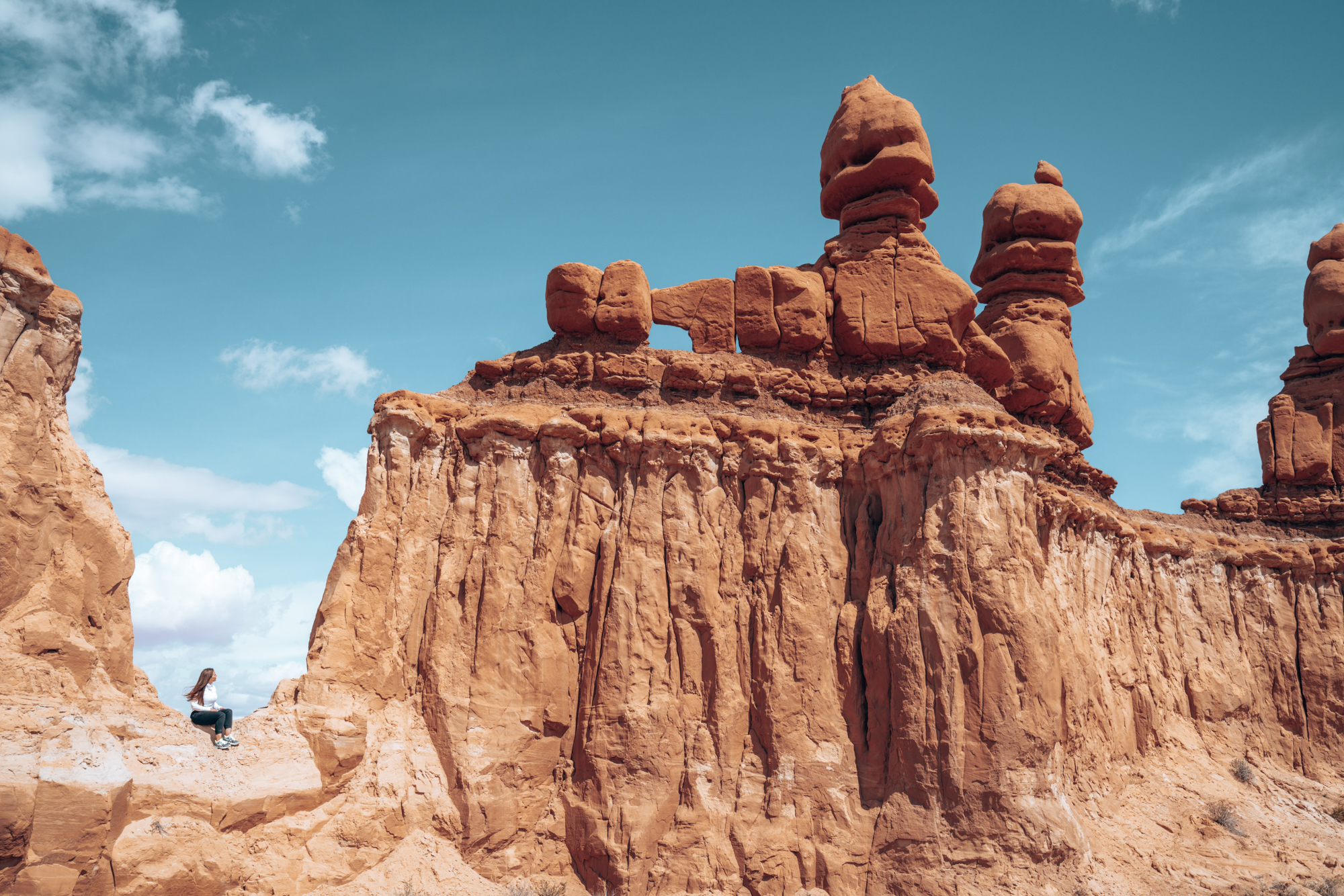 a woman sits at the ledge next to a big red butte called three sisters. 