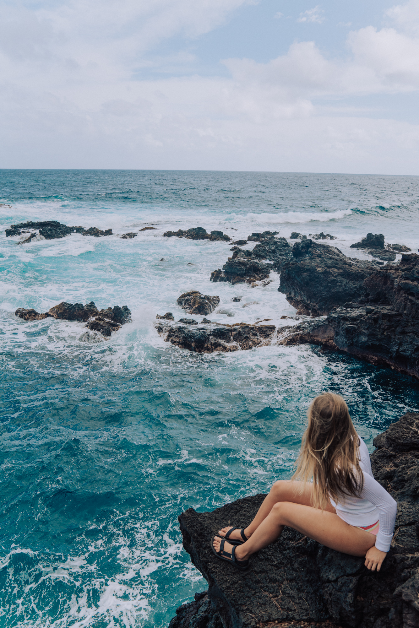 woman overlooking the ocean below from a cliff.