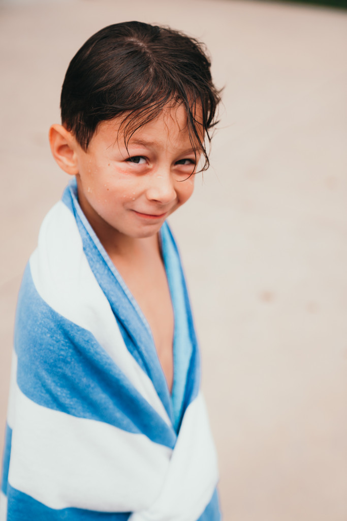 A little boy is wrapped up in a blue and white pool towel. 