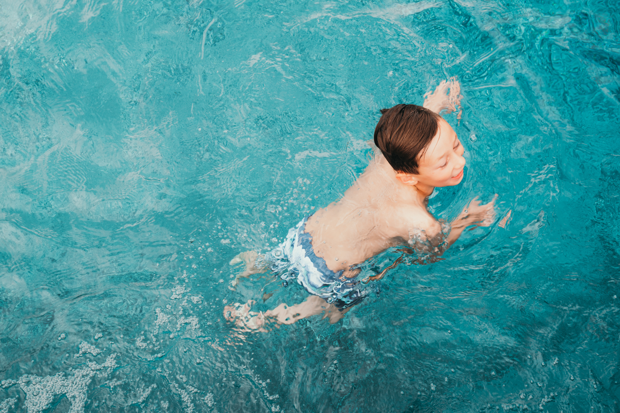 A little boy swims in a backyard swimming pool.