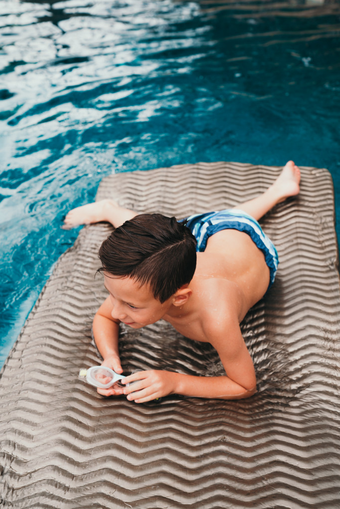 A little boy swims in a backyard swimming pool.