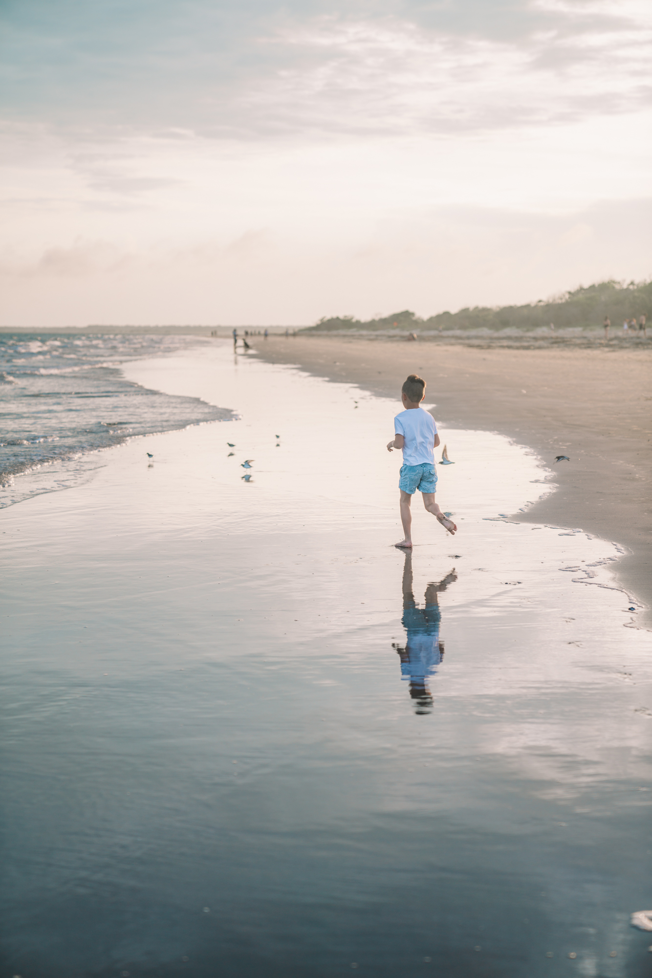 Things to do in Charleston sc with kids - A little boy runs along the shore on the beach - his reflection can be seen in the water. 