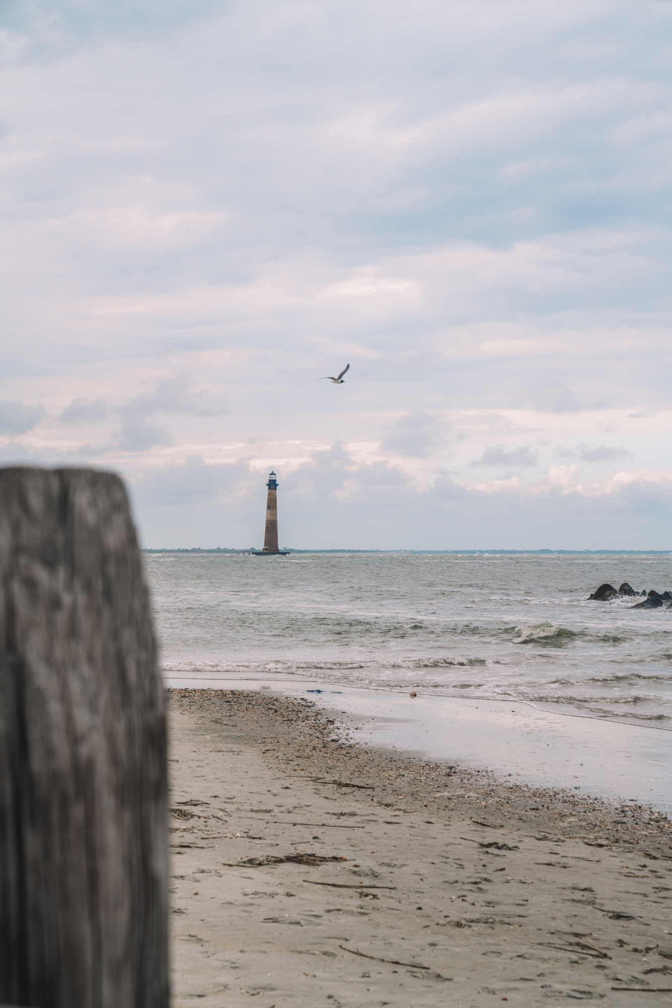 A red and white lighthouse stands far away with the beach in the foreground.