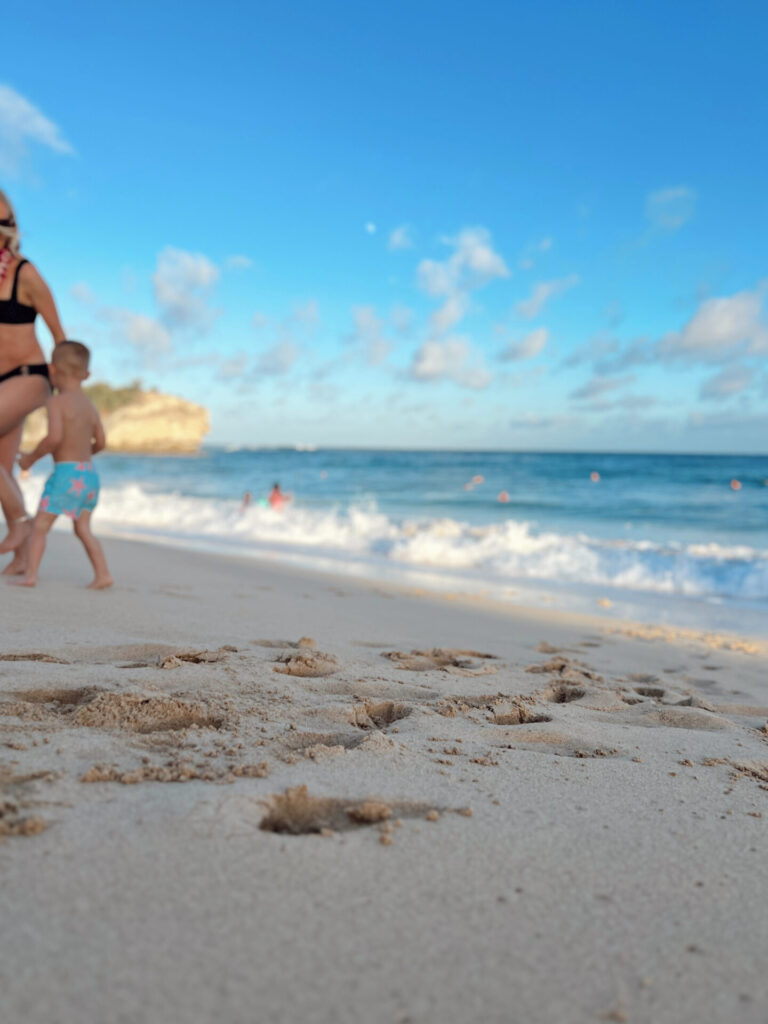 Mom and toddler walk a white-sand beach on a family vacation booked with World of Hyatt points