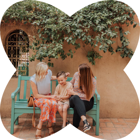 Kam with two children sitting on turquoise bench under ivy covered wall in Moroccan courtyard