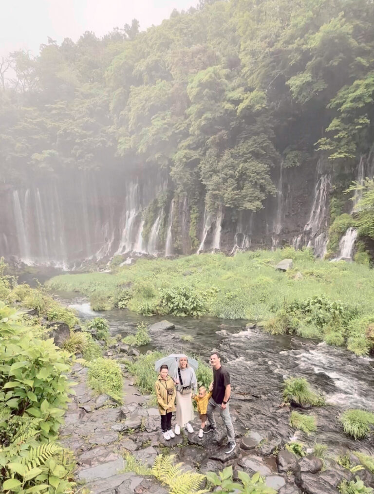 Family of four standing in front of Shiraito waterfall cascade in Japan