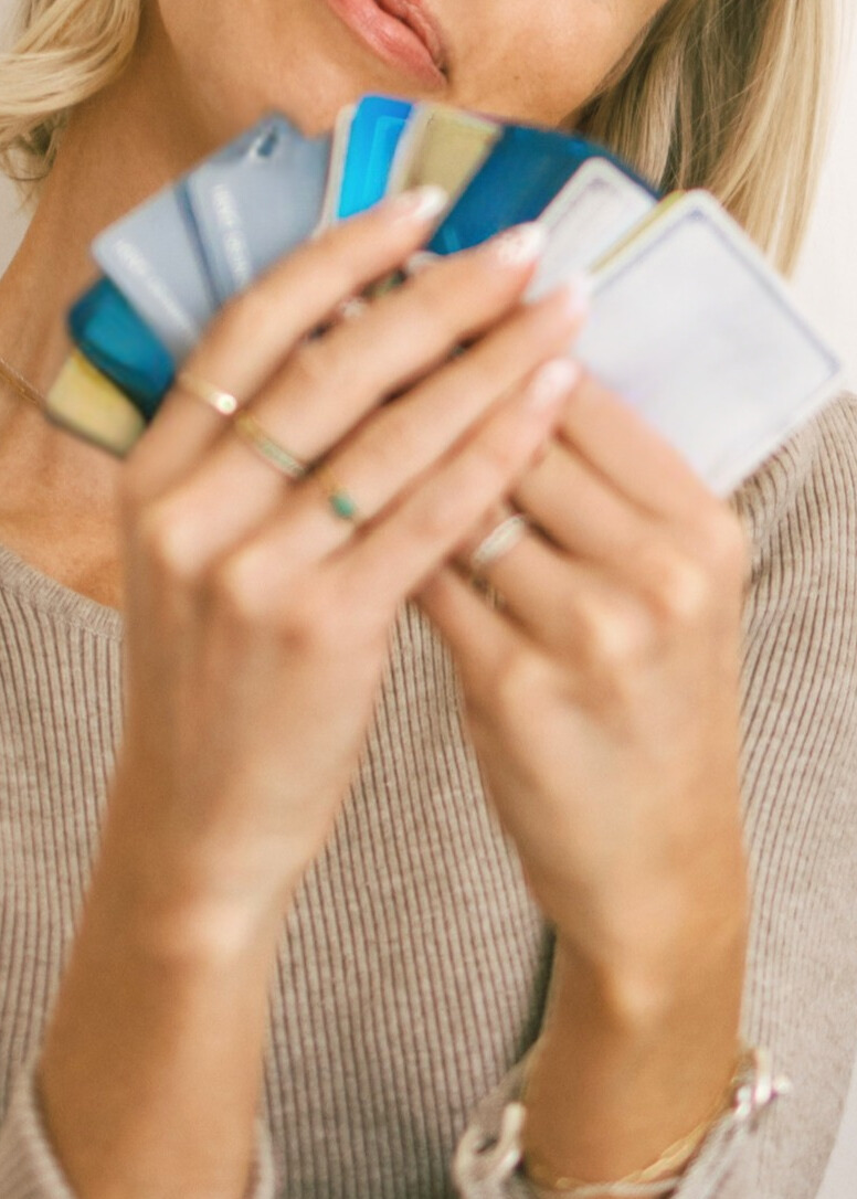 Kam sitting on stool holding gold credit card over face