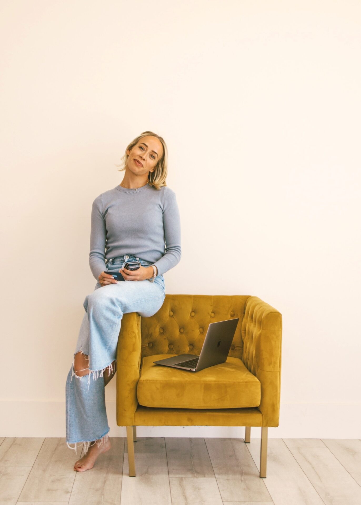 Kam sitting on yellow velvet chair holding multiple travel credit cards