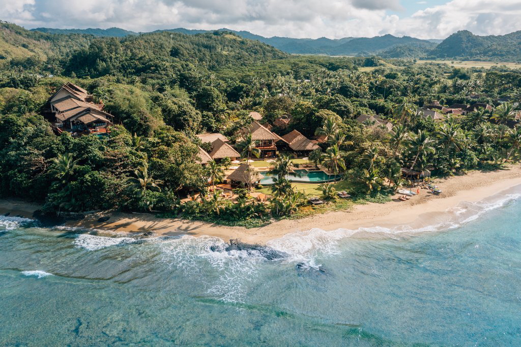 Aerial view of Nanuku Resort Fiji showing luxury beachfront villas and traditional Fijian architecture booked through Amex Fine Hotels and Resorts