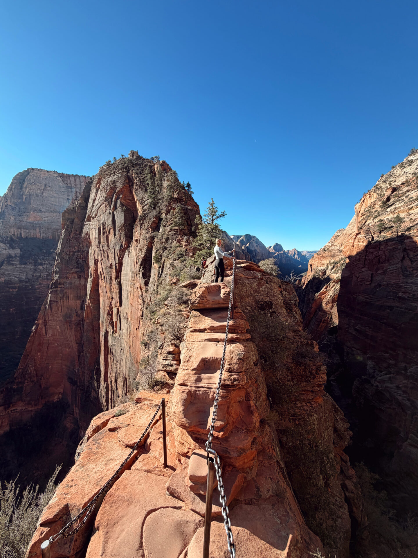 Woman hiking along the chains section of Angels Landing in Zion National Park with sheer canyon drops on either side