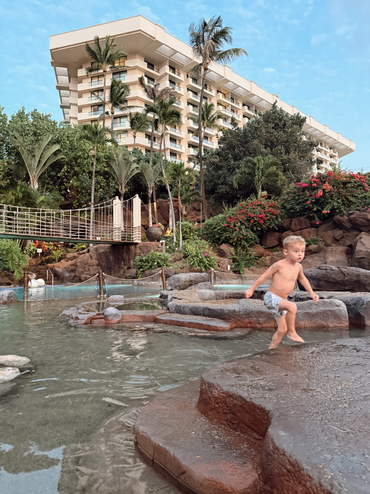 Toddler exploring the rock pool area at the Hyatt Regency Maui with the resort tower behind