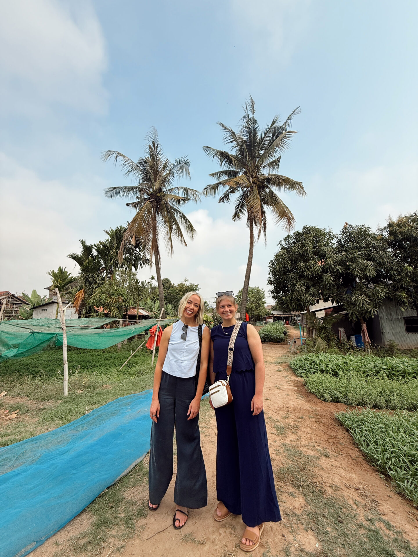 Two travelers standing in the Cambodian countryside with palm trees and rural scenery