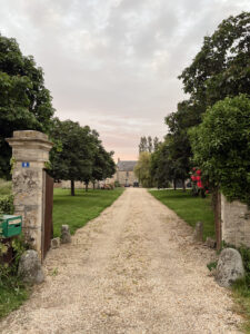Stone gate and gravel driveway leading to French farmhouse Airbnb at sunset