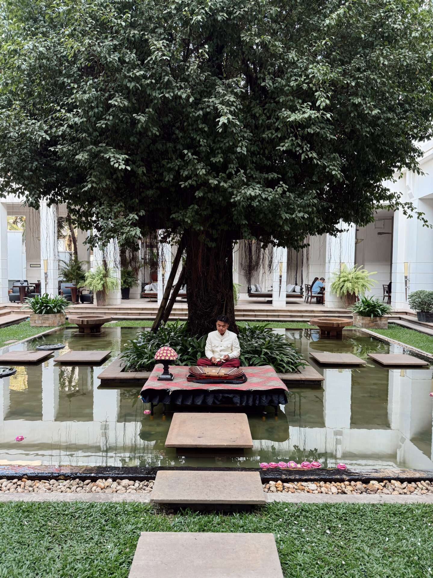 Traditional Cambodian musician playing a wooden instrument on a platform in the Park Hyatt Siem Reap courtyard pond