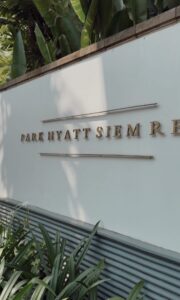 Gold lettering Park Hyatt Siem Reap sign on the hotel exterior wall surrounded by tropical greenery