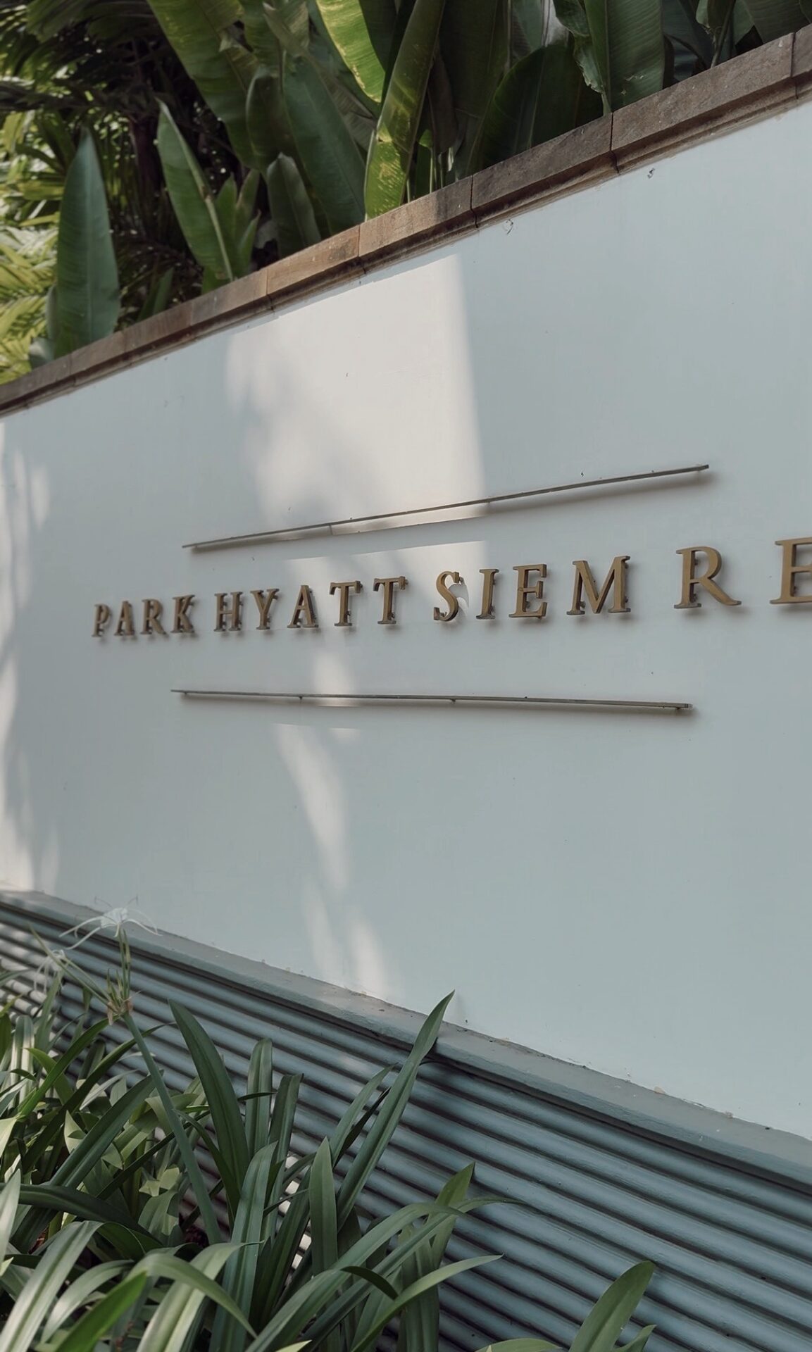Gold lettering Park Hyatt Siem Reap sign on the hotel exterior wall surrounded by tropical greenery