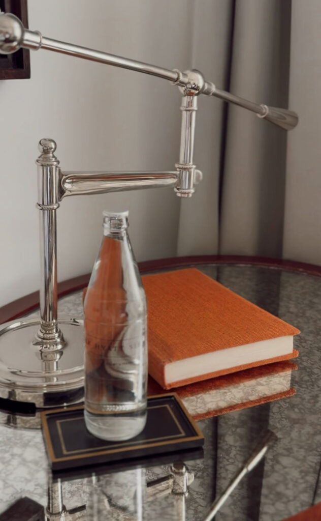 Elegant bedside table with silver lamp, glass water bottle, and orange linen book in a Park Hyatt Siem Reap guest room