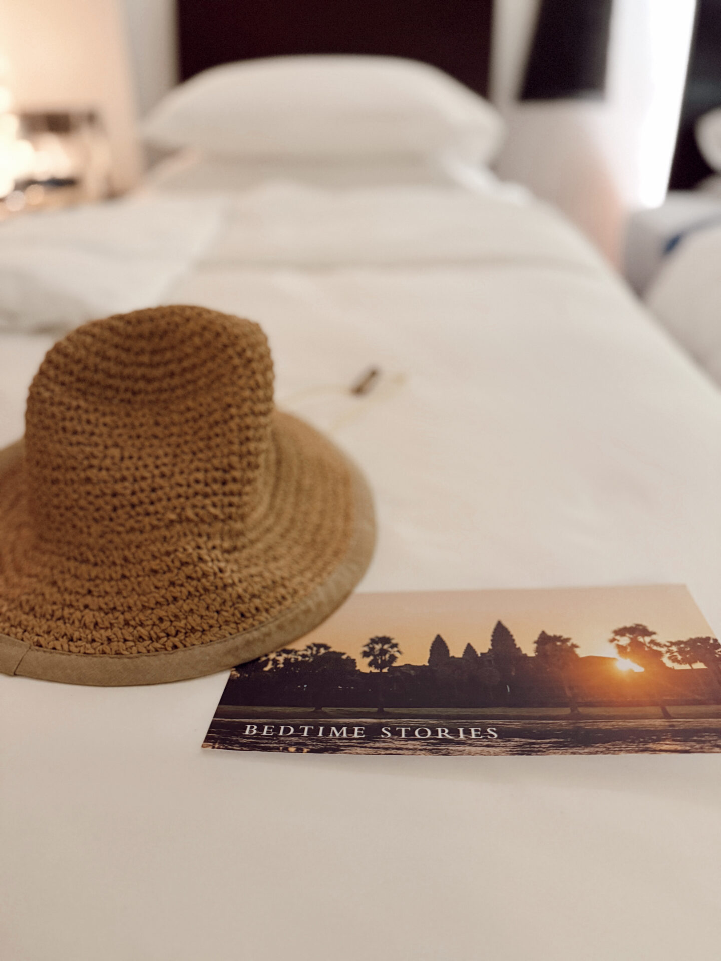 Straw sun hat and Bedtime Stories card with Angkor Wat sunset on a white hotel bed at Park Hyatt Siem Reap