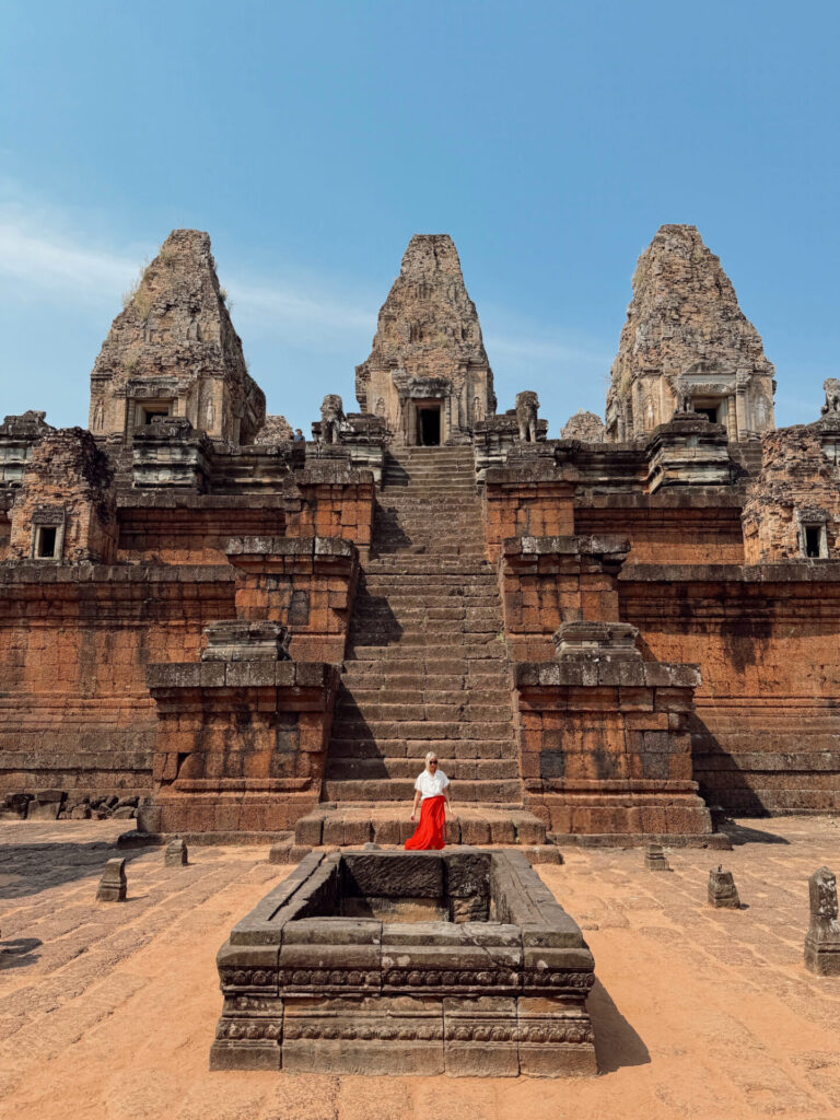Woman in red skirt standing on the sandstone steps of Pre Rup temple in Siem Reap