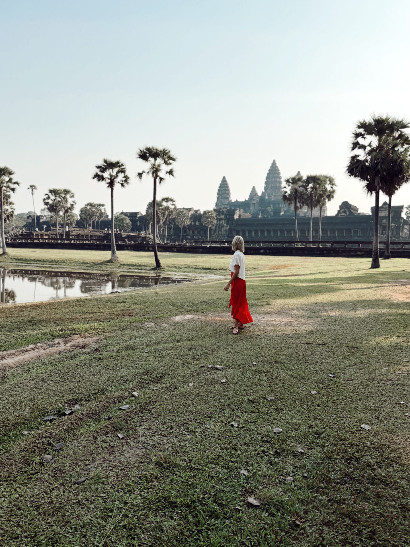 Woman in a red skirt walking across the lawn toward Angkor Wat temple at sunrise in Siem Reap Cambodia