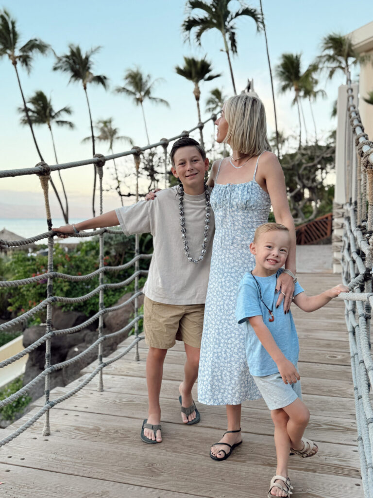 A mom and two boys on a rope bridge lined with palm trees at sunset at the Hyatt Regency Maui.