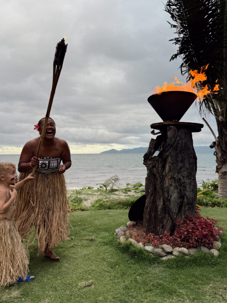 Nanuku staff member laughing during a sunset torch lighting ceremony as a young boy watches