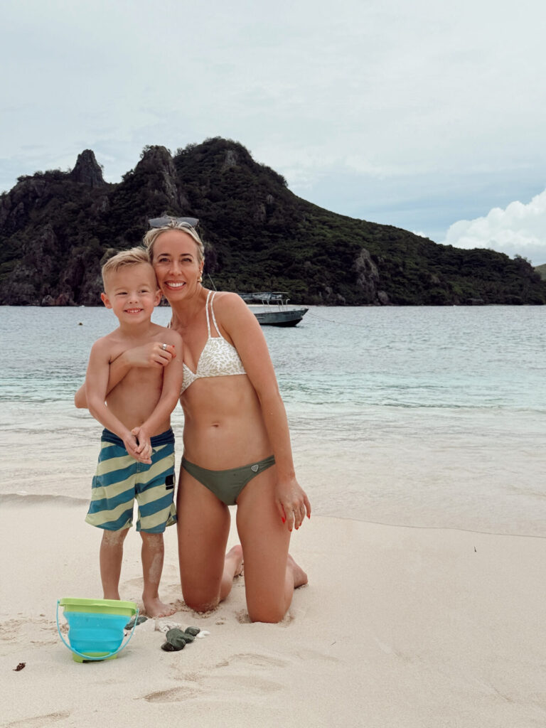 Mom and young son on a white sand Mamanuca Islands beach with a dramatic green peak behind them
