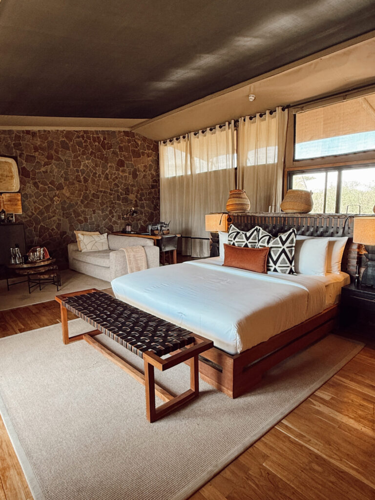Luxury tented suite at Mapito Safari Camp in the Serengeti with a king bed, stone wall, and woven bench