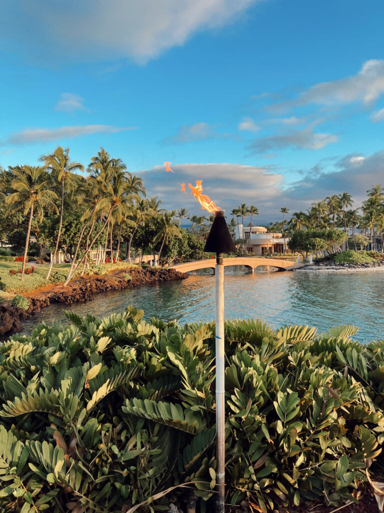 Lit tiki torch at dusk overlooking the lagoon and stone bridge at a hilton waikoloa village