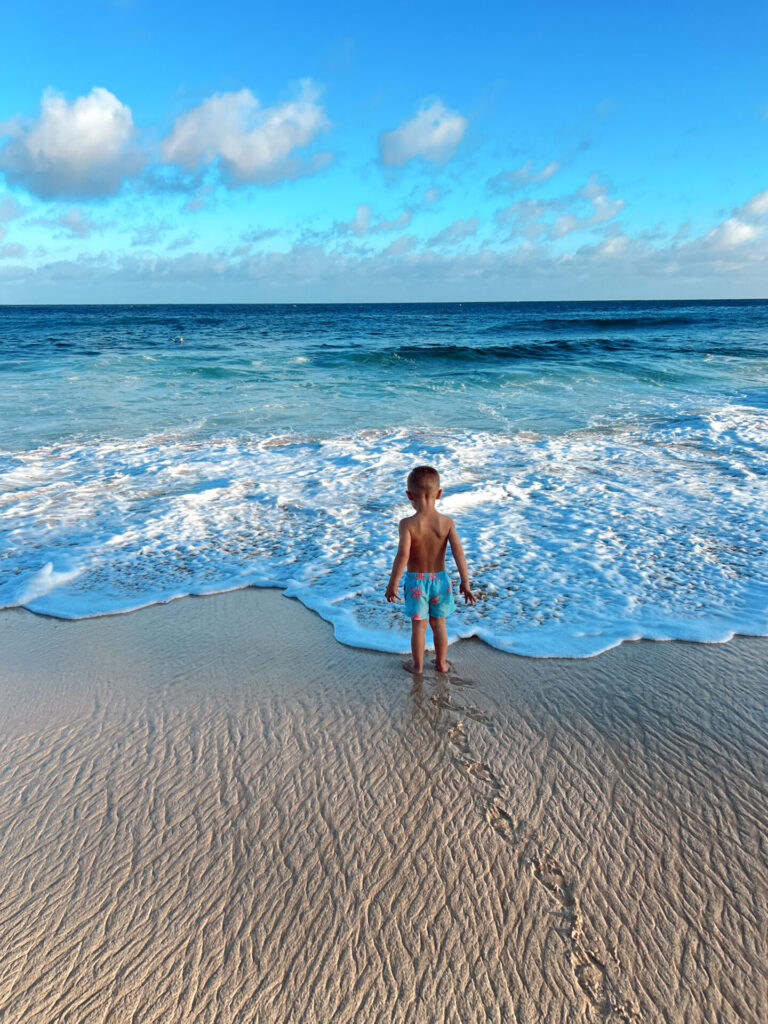 Toddler standing at the shoreline as waves wash in on a beach in Hawaii